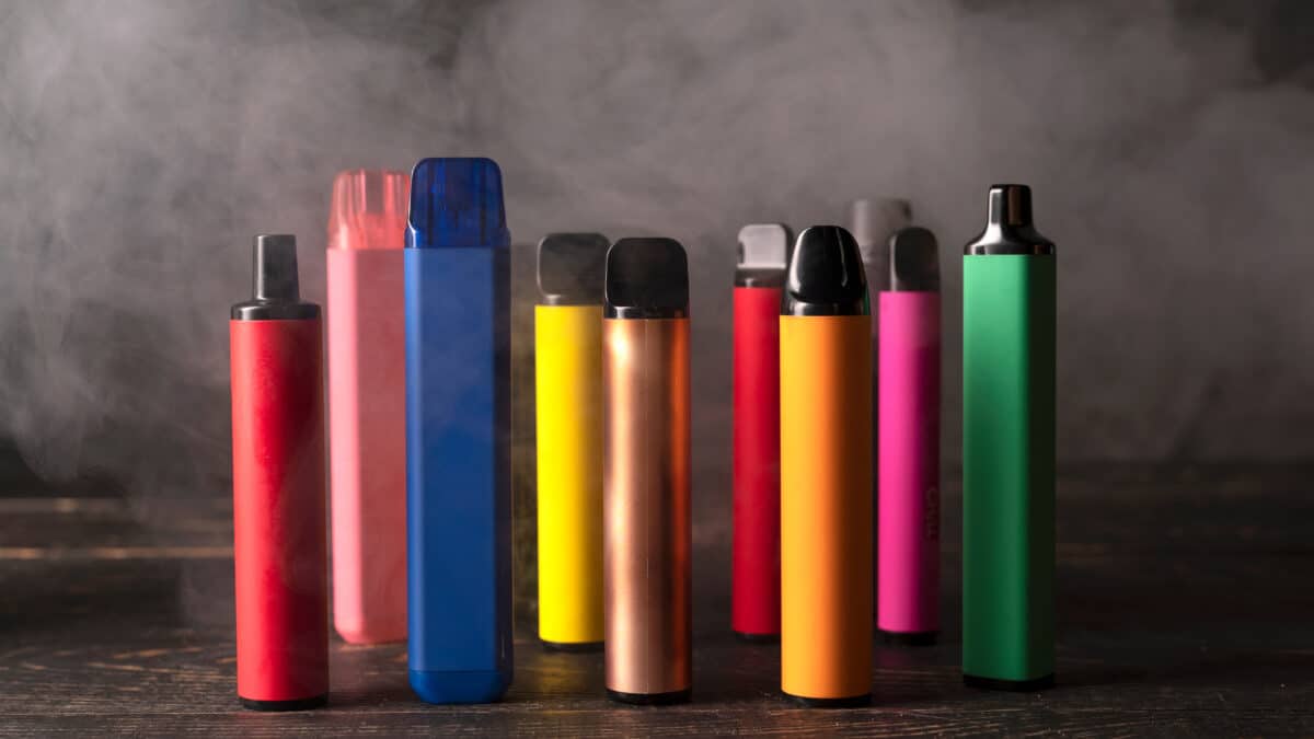 Set of colorful disposable electronic cigarettes on a dark wood background with smoke.